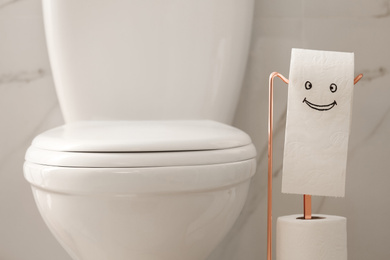 Photo of Modern toilet bowl and paper with funny face in bathroom