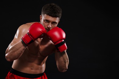 Photo of Man in boxing gloves on black background. Space for text