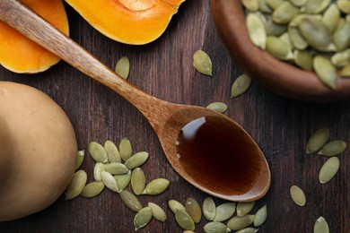 Photo of Spoon with oil and pumpkin seeds on wooden table, flat lay