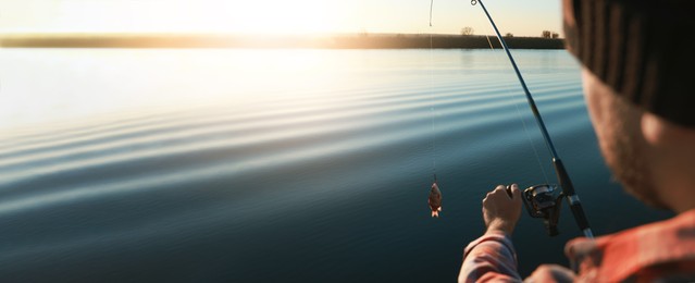 Image of Fisherman catching fish with rod at riverside, closeup view with space for text. Banner design
