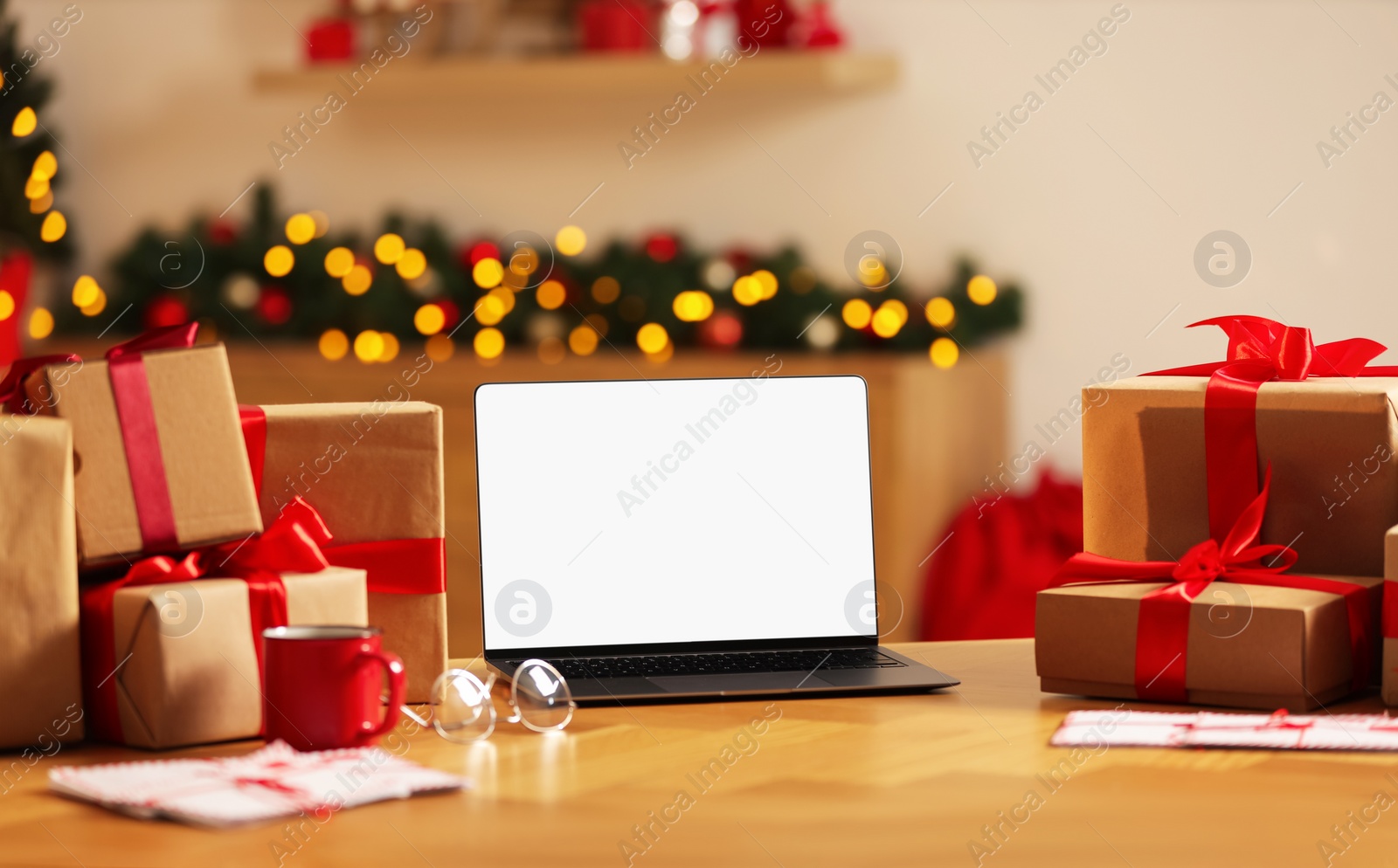 Photo of Christmas time. Laptop with blank screen, gift boxes and letters on table at home