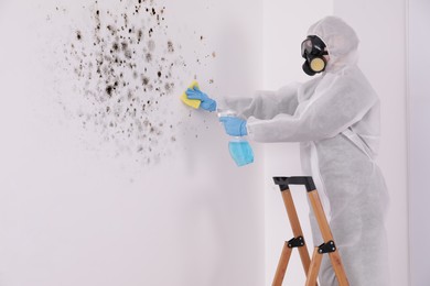 Image of Woman in protective suit and rubber gloves using mold remover and rag on wall