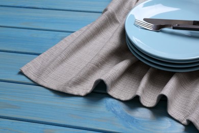 Photo of Clean kitchen towel and stack of plates with cutlery on blue wooden table