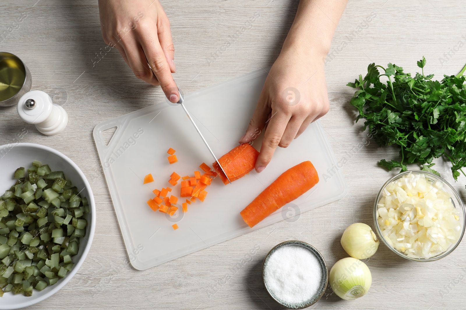 Photo of Woman cutting boiled carrot at white wooden table, top view. Cooking vinaigrette salad