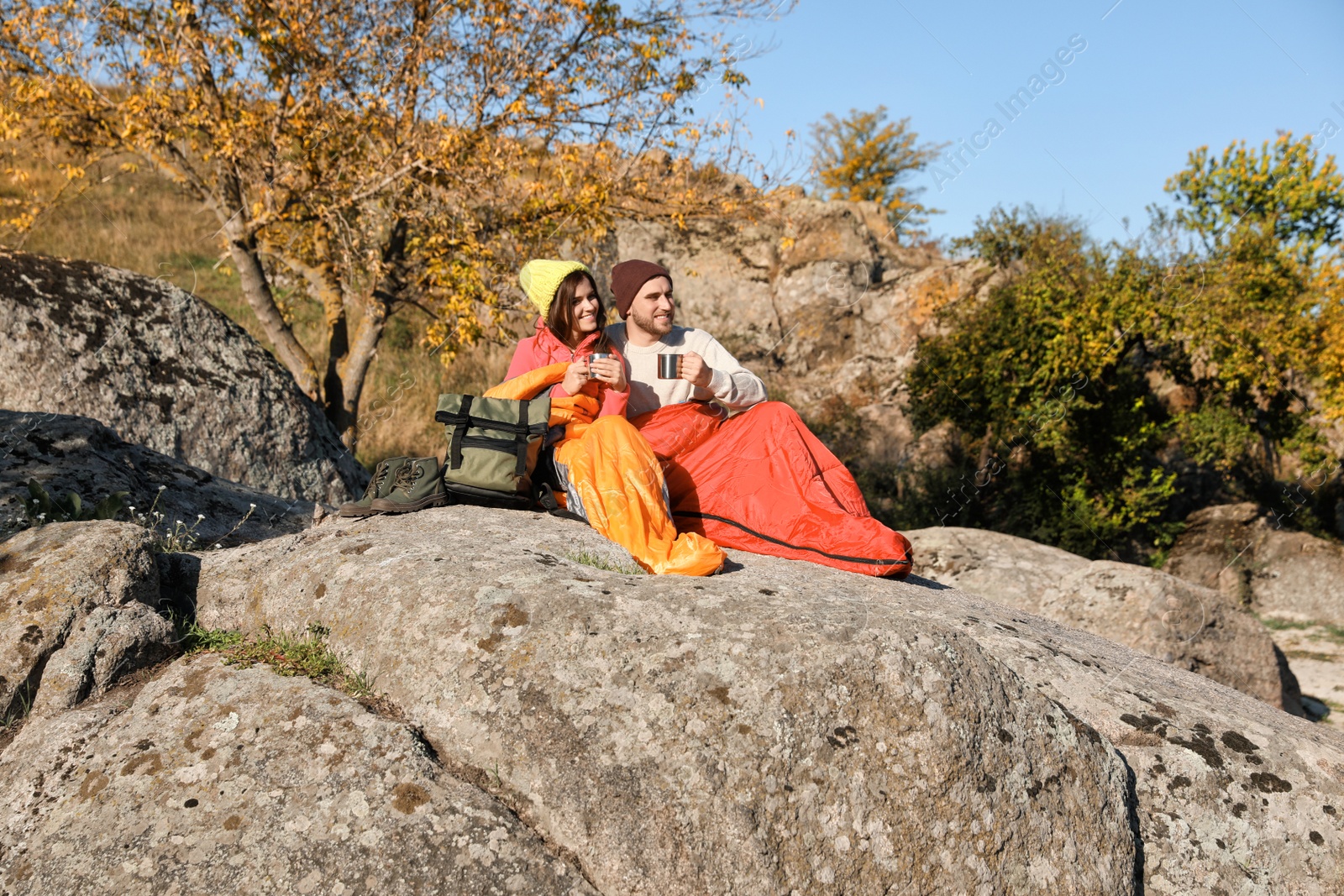 Photo of Couple of campers in sleeping bags sitting on rock