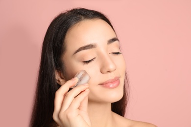 Young woman with ice cube on color background. Skin care