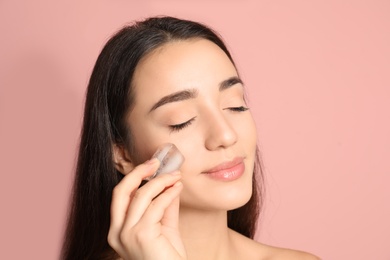 Photo of Young woman with ice cube on color background. Skin care