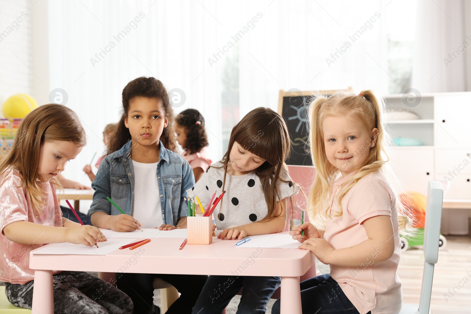 Photo of Adorable children drawing together at table indoors. Kindergarten playtime activities