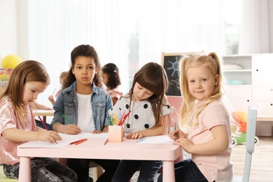 Photo of Adorable children drawing together at table indoors. Kindergarten playtime activities