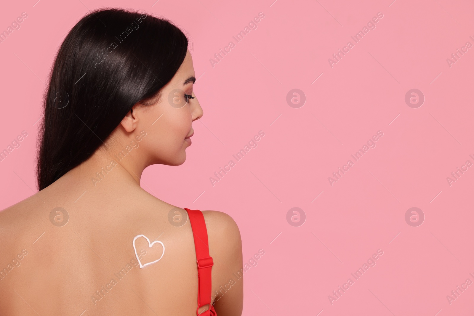 Photo of Young woman with sun protection cream on her back against pink background. Space for text