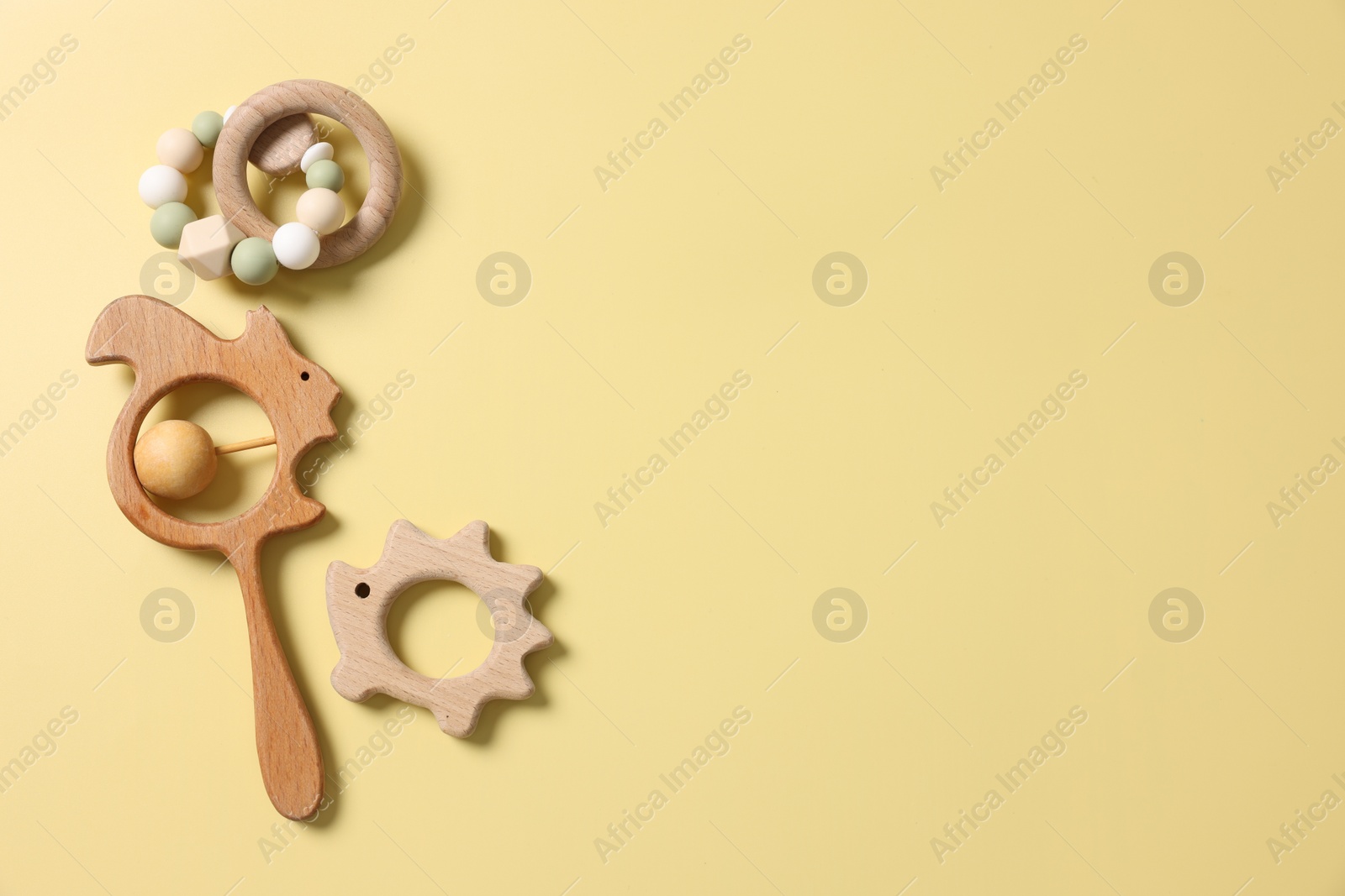 Photo of Baby accessories. Wooden rattles on yellow background, flat lay. Space for text