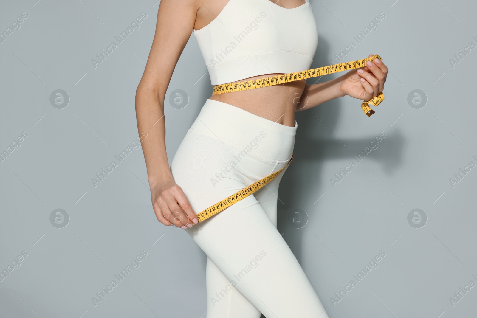 Photo of Young woman measuring waist with tape on grey background, closeup