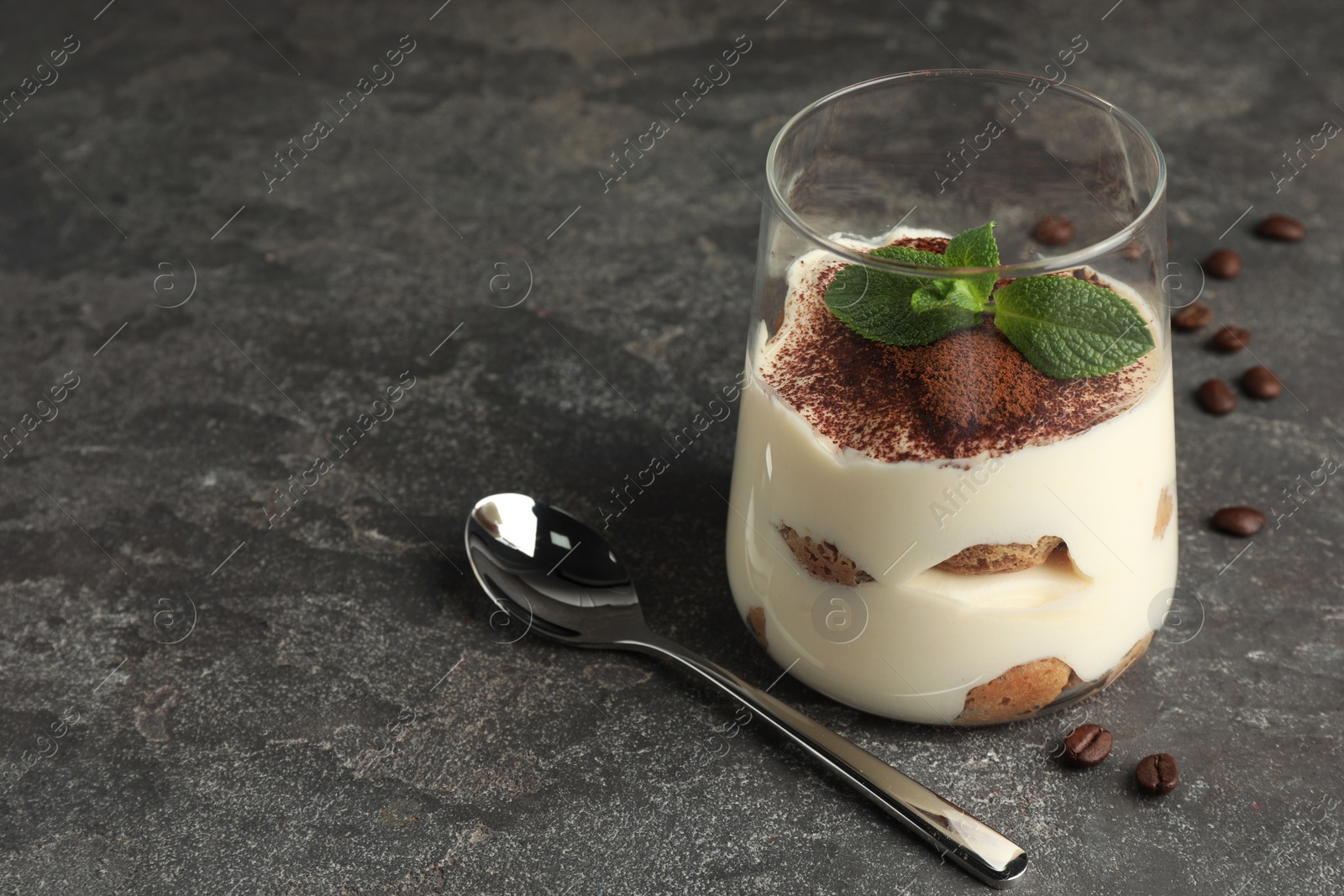 Photo of Delicious tiramisu with mint in glass on grey table. Space for text