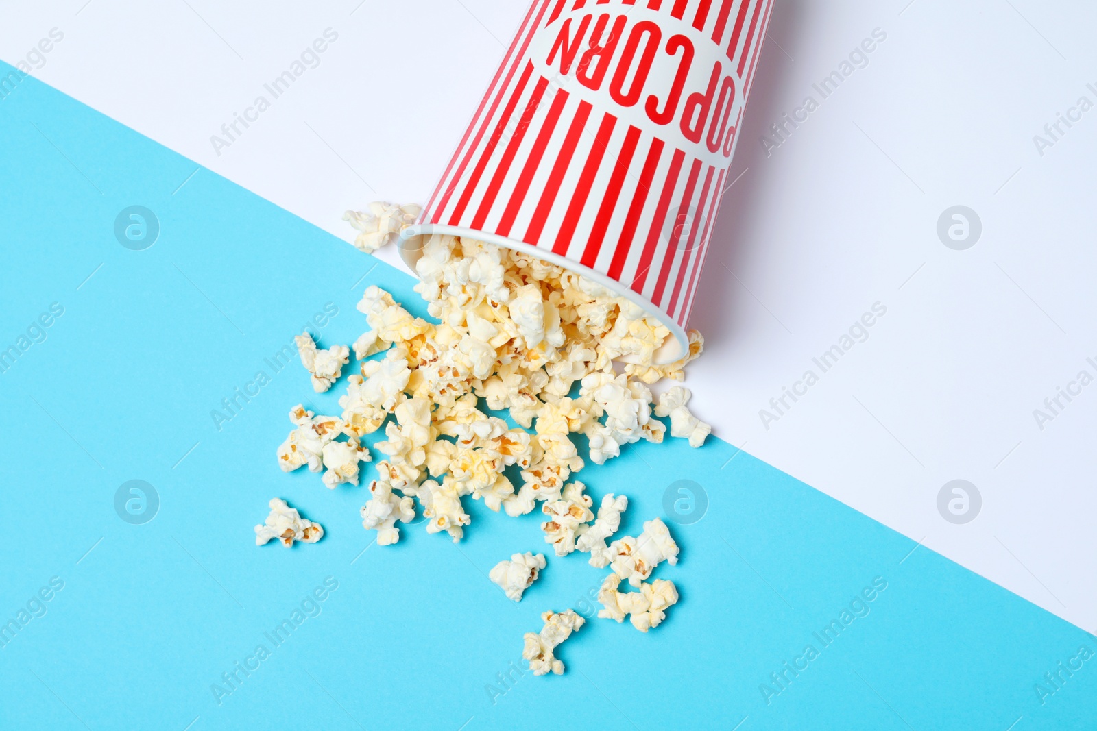 Photo of Overturned paper cup with tasty popcorn on color background, top view