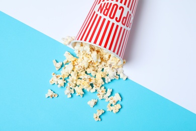 Overturned paper cup with tasty popcorn on color background, top view