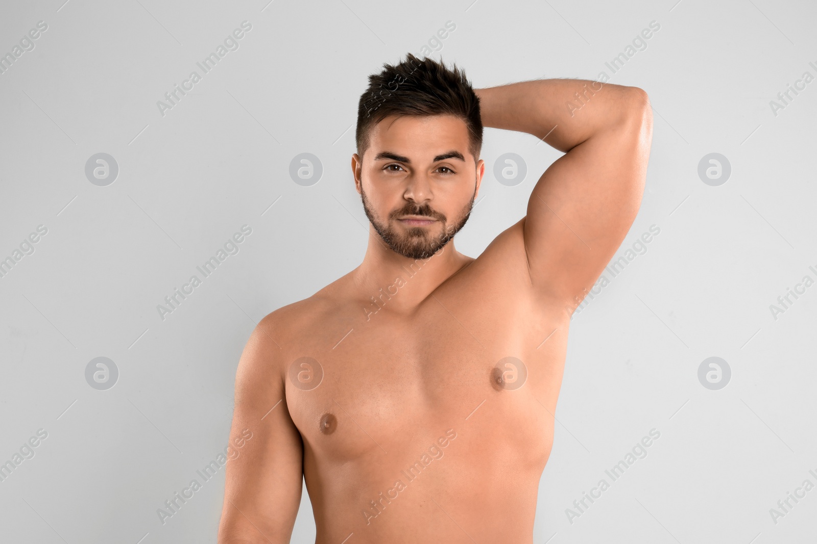 Photo of Young man showing hairless armpit after epilation procedure on light grey background