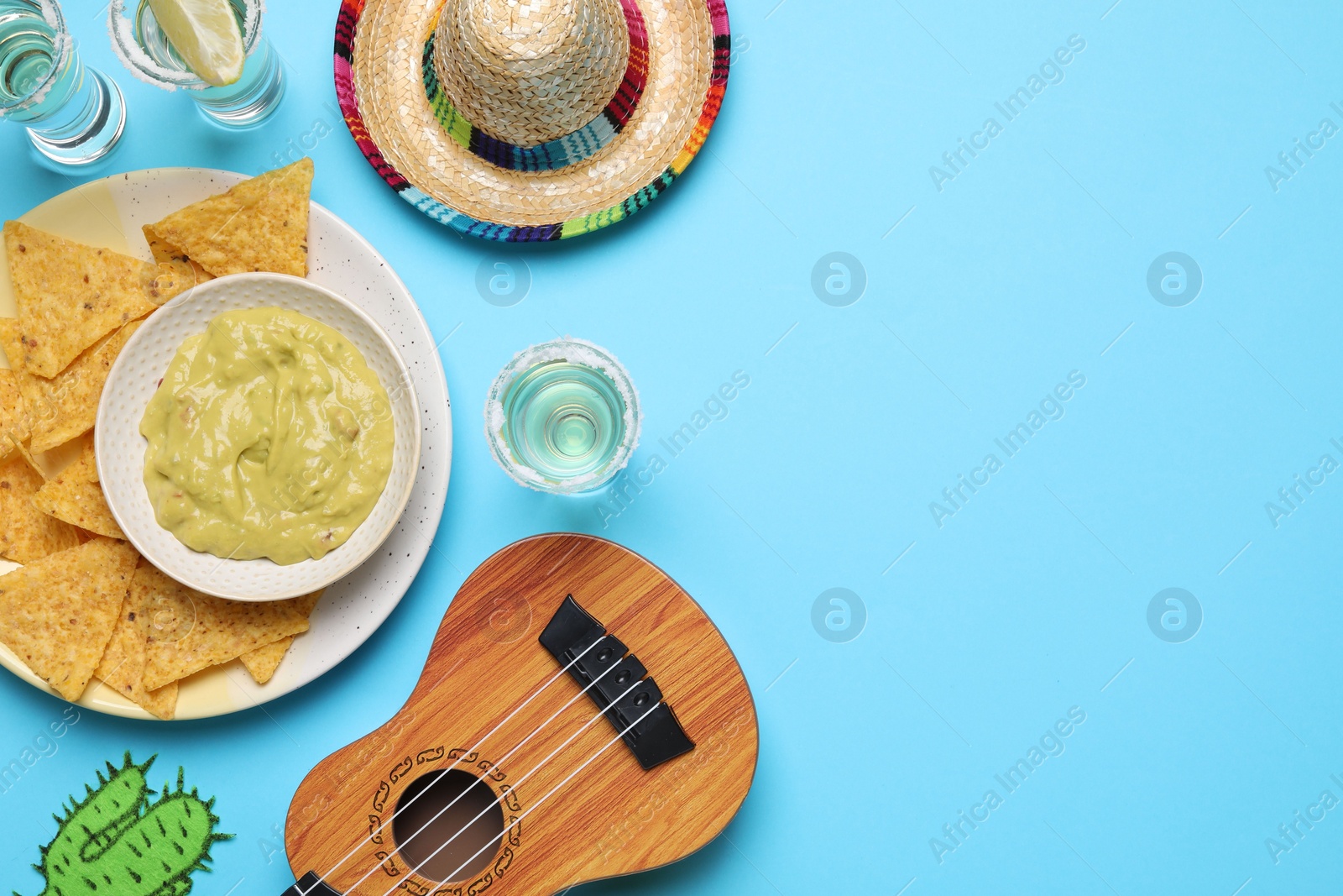 Photo of Mexican sombrero hat, ukulele, tequila, nachos chips, guacamole and paper cactus on light blue background, flat lay. Space for text