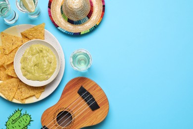 Mexican sombrero hat, ukulele, tequila, nachos chips, guacamole and paper cactus on light blue background, flat lay. Space for text