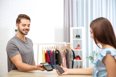 Photo of Woman using terminal for contactless payment with smartphone in shop