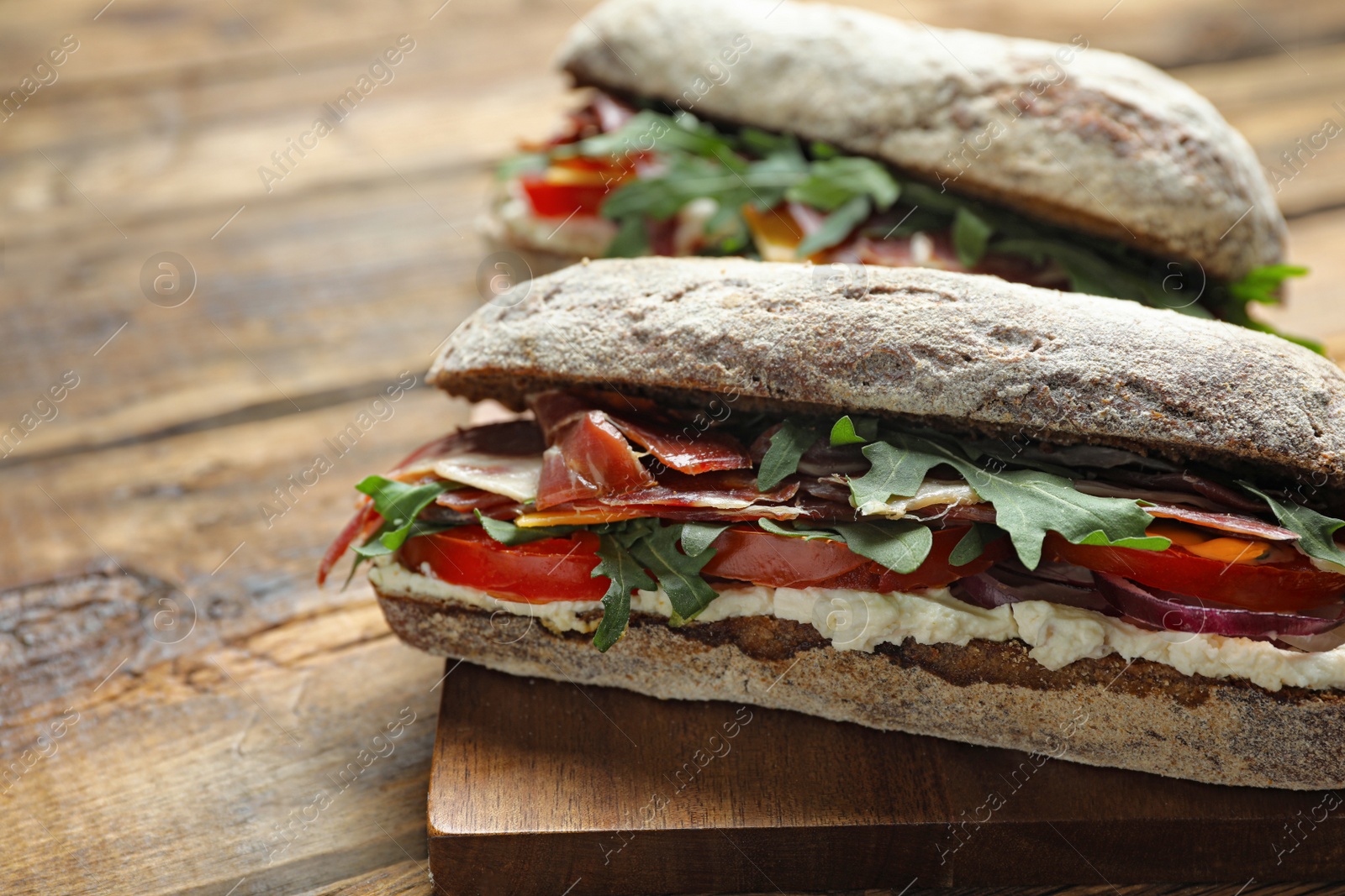 Photo of Delicious sandwiches with fresh vegetables and prosciutto on wooden table, closeup