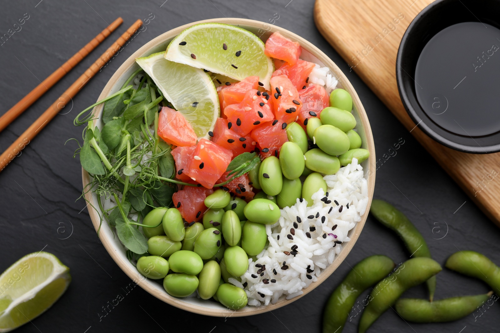 Photo of Delicious poke bowl with lime, fish and edamame beans on black table, flat lay