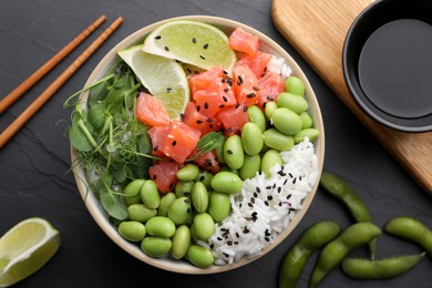 Photo of Delicious poke bowl with lime, fish and edamame beans on black table, flat lay