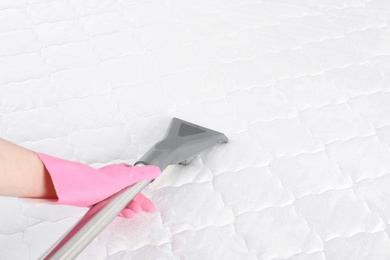 Photo of Woman disinfecting mattress with vacuum cleaner, closeup. Space for text