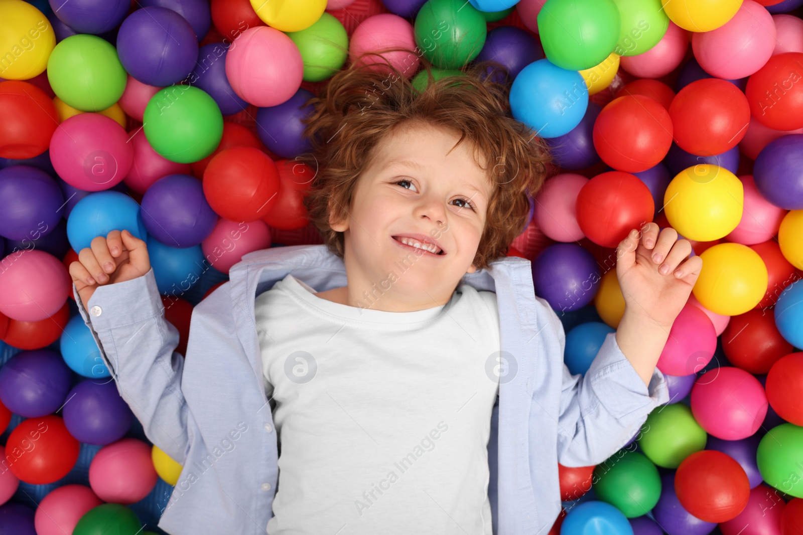 Photo of Happy little boy lying on many colorful balls, top view