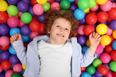 Happy little boy lying on many colorful balls, top view