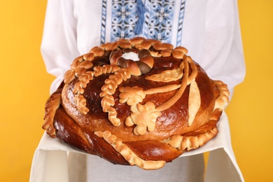 Photo of Woman with korovai on yellow background, closeup. Ukrainian bread and salt welcoming tradition