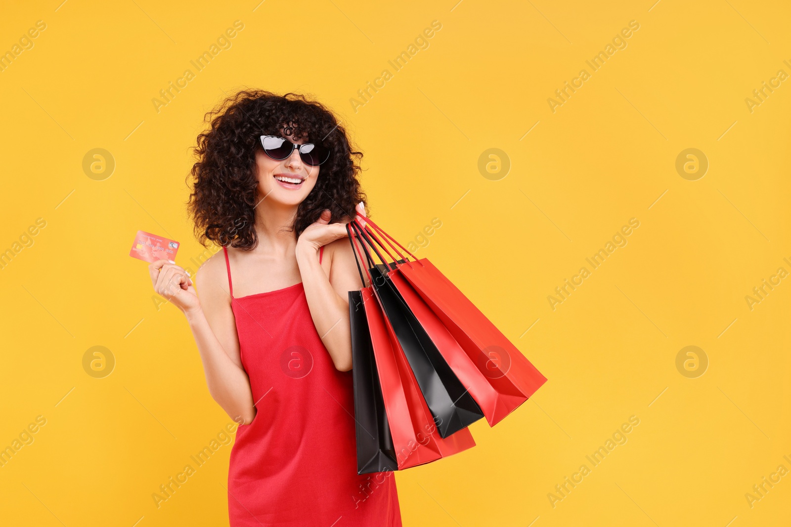 Photo of Happy young woman with shopping bags and credit card on yellow background. Space for text