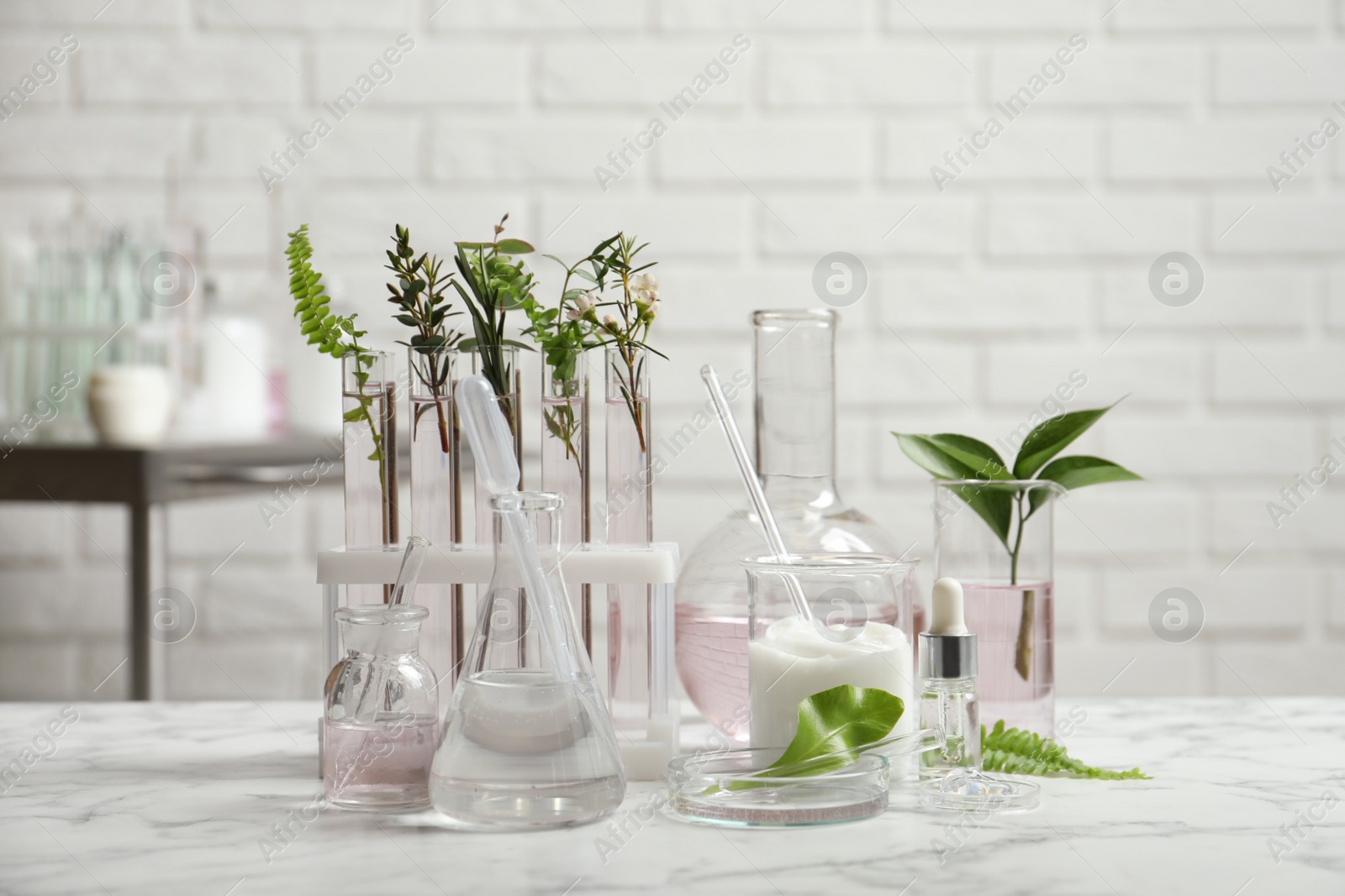 Photo of Natural ingredients and laboratory glassware for organic cosmetic product on white marble table