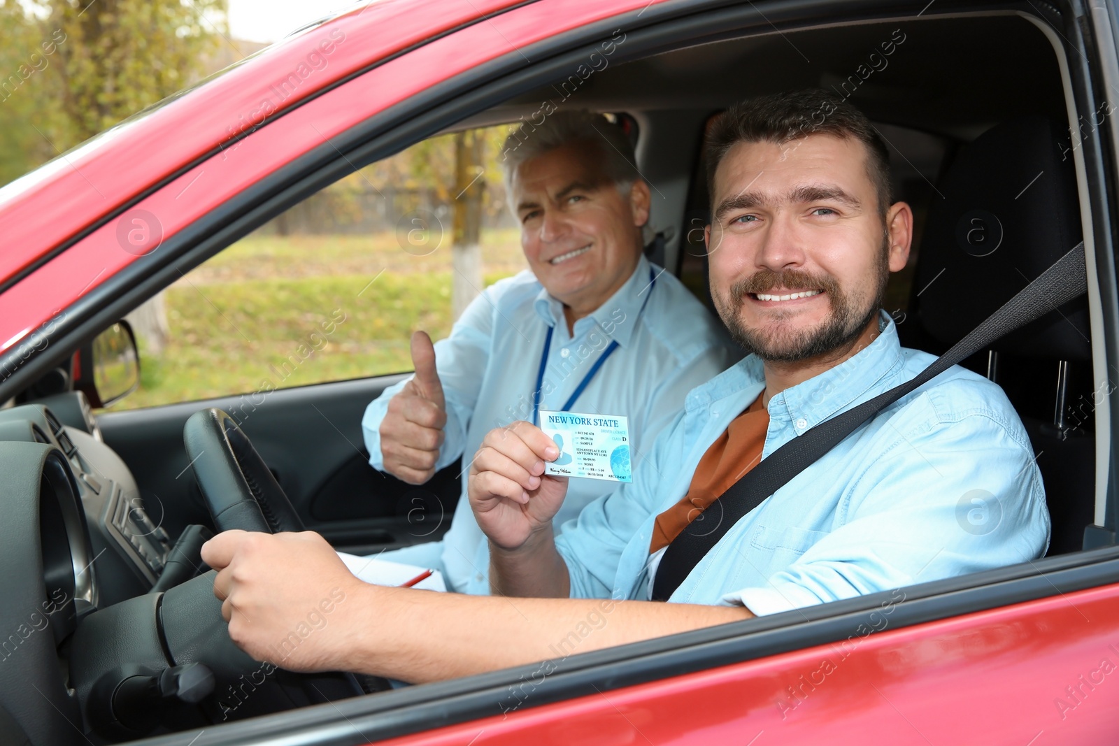 Photo of Instructor near happy man showing driving license in car