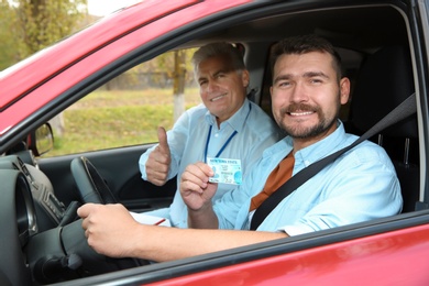 Photo of Instructor near happy man showing driving license in car