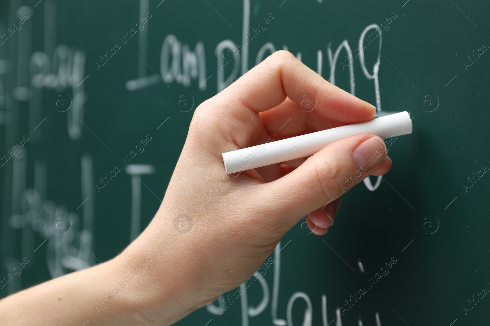 Photo of English teacher writing with chalk on green chalkboard, closeup