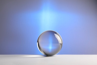 Photo of Transparent glass ball on table against blue background