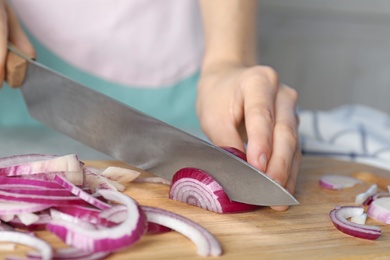 Photo of Woman cutting fresh red onion on wooden board, closeup