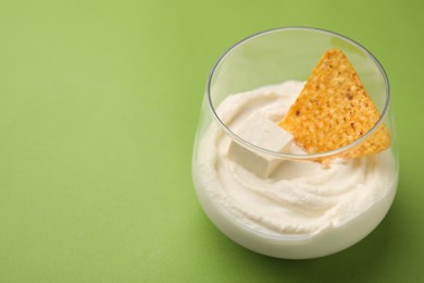 Delicious tofu sauce served with nachos chip on green background, closeup. Space for text