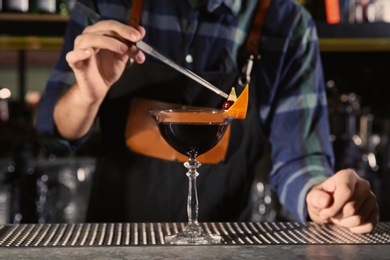 Photo of Barman decorating alcoholic cocktail at counter in night club, closeup