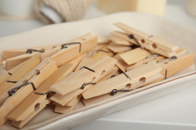 Many wooden clothespins in bowl on white table, closeup