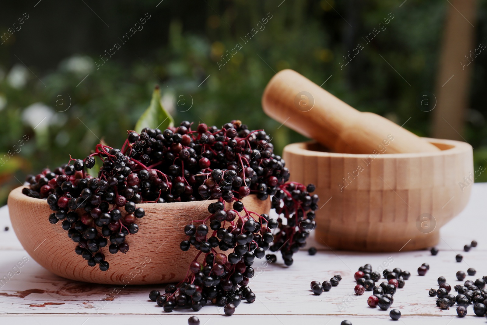 Photo of Tasty elderberries (Sambucus) on white wooden table outdoors