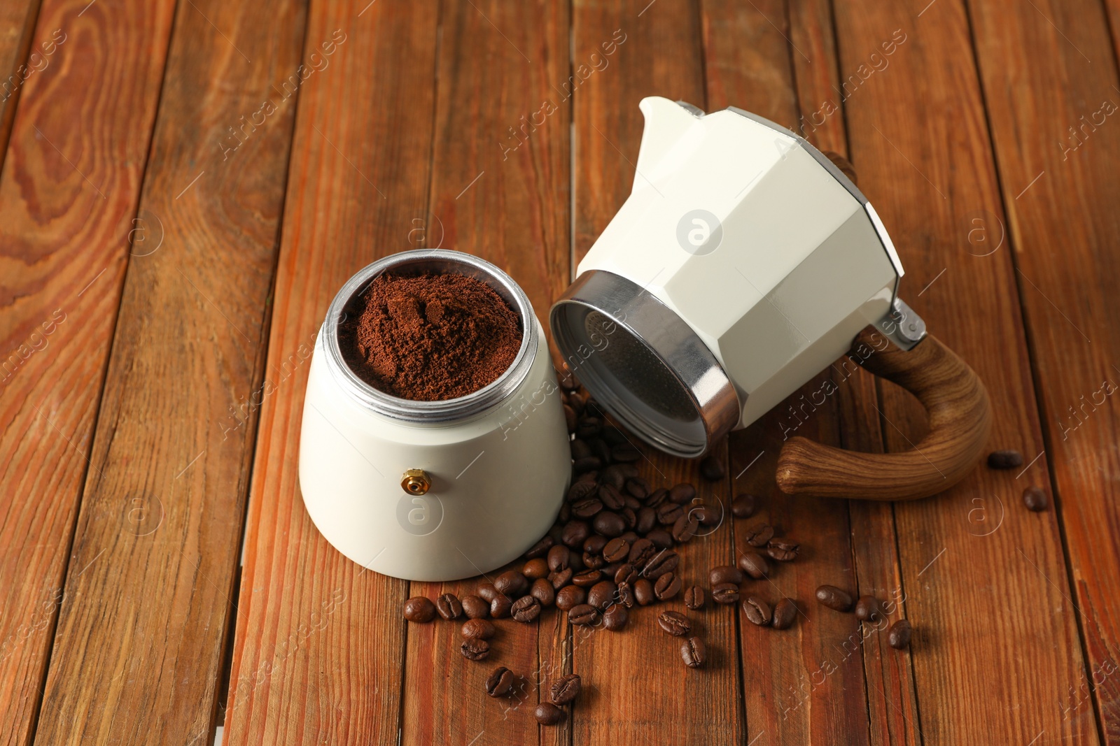 Photo of Moka pot with ground coffee and beans on wooden table