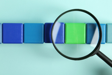 Photo of Magnifying glass and colorful cubes on light blue background, top view. Search concept