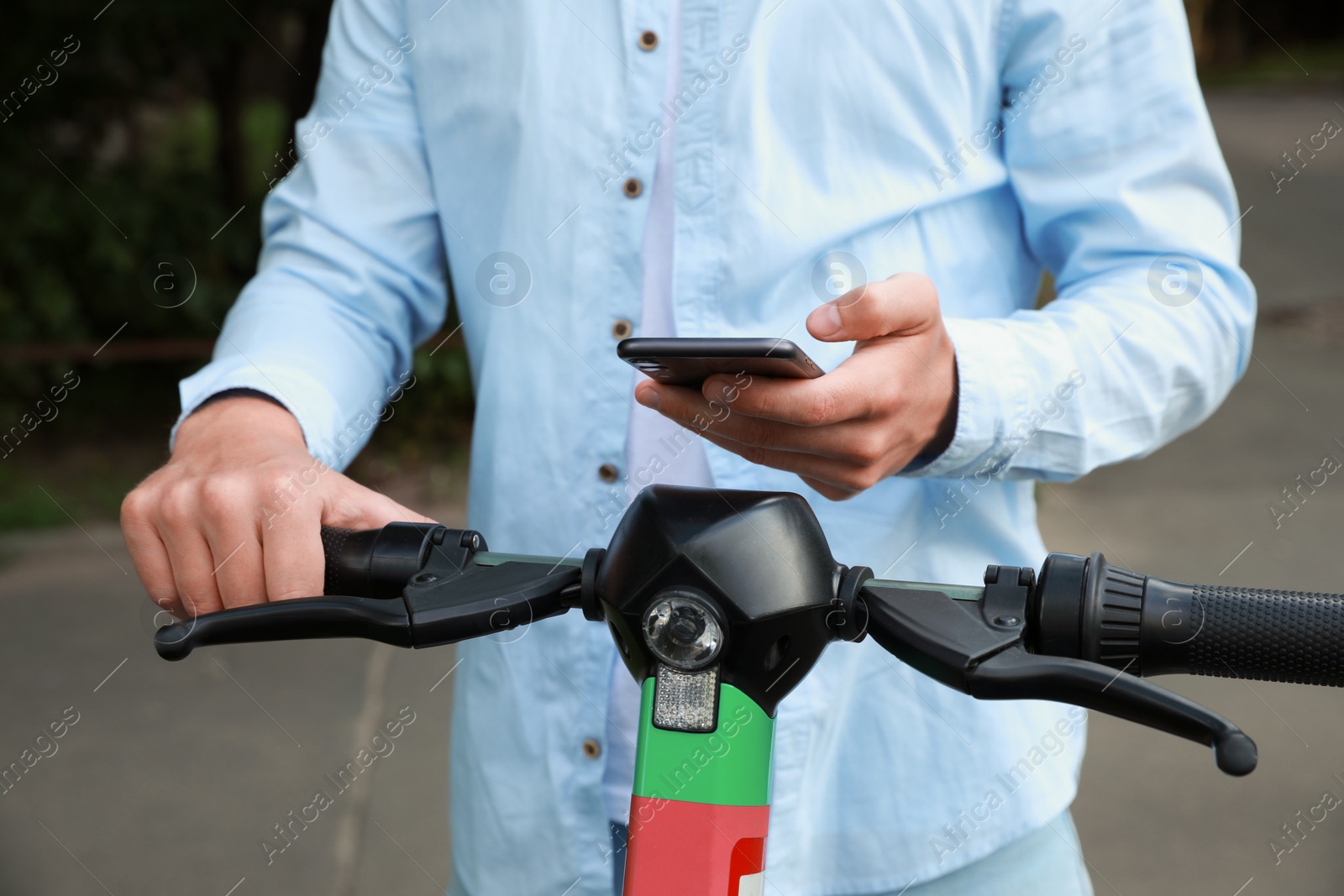 Photo of Man using smartphone to pay and unblock electric kick scooter outdoors, closeup