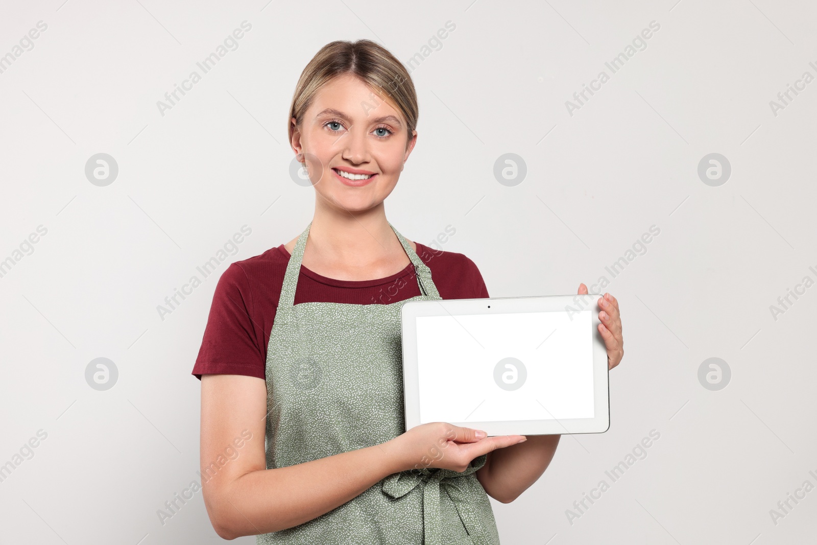 Photo of Beautiful young woman in clean apron with tablet on light grey background