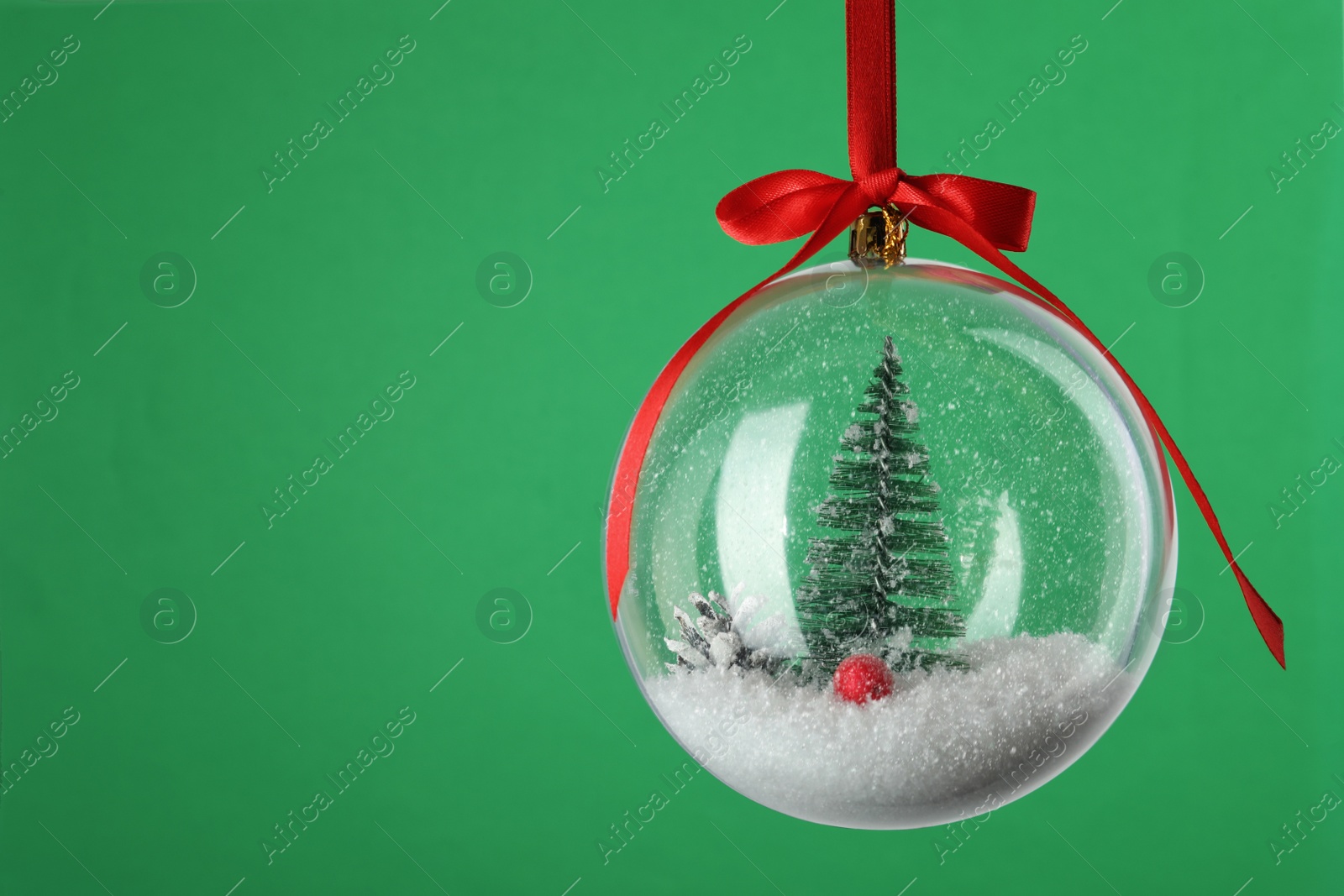 Photo of Beautiful Christmas snow globe hanging on green background, closeup. Space for text