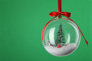 Photo of Beautiful Christmas snow globe hanging on green background, closeup. Space for text