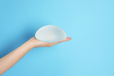 Photo of Woman holding silicone implant for breast augmentation on color background, space for text. Cosmetic surgery