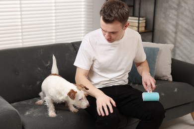 Photo of Pet shedding. Man with lint roller removing dog's hair from pants at home