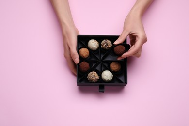 Woman taking chocolate candy out of box on pink background, top view